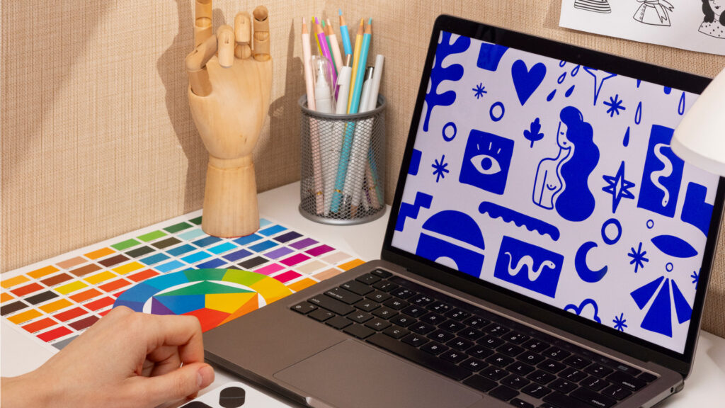 Persona haciendo diseños en un ordenador con material de referencia en la mesa