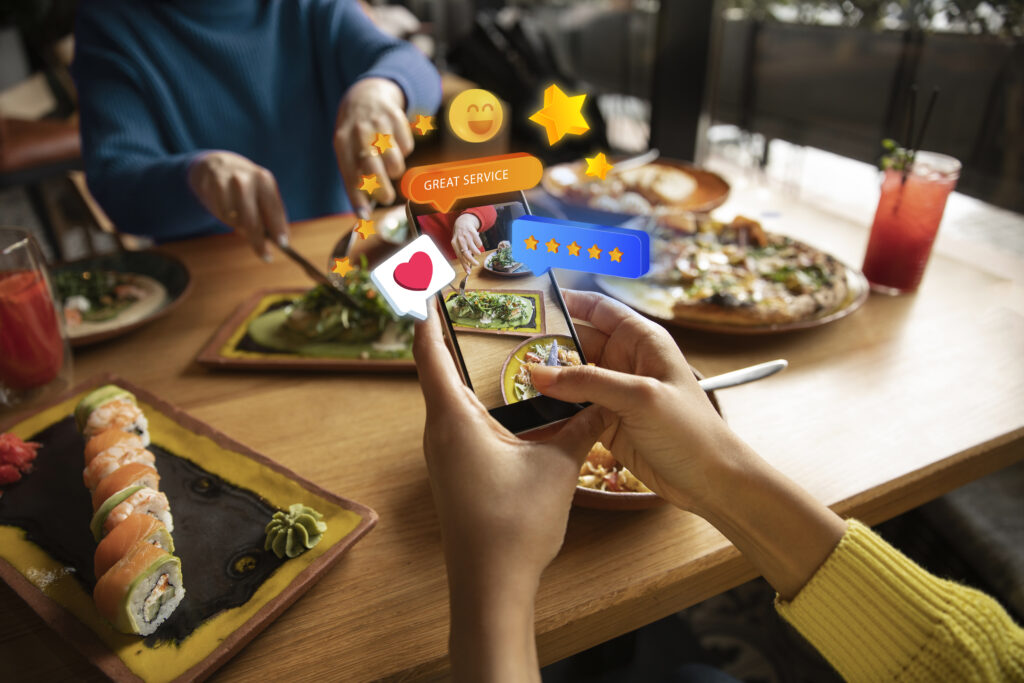 Persona en un restaurante con el móvil del que sale multitud de emoticonos de valoración